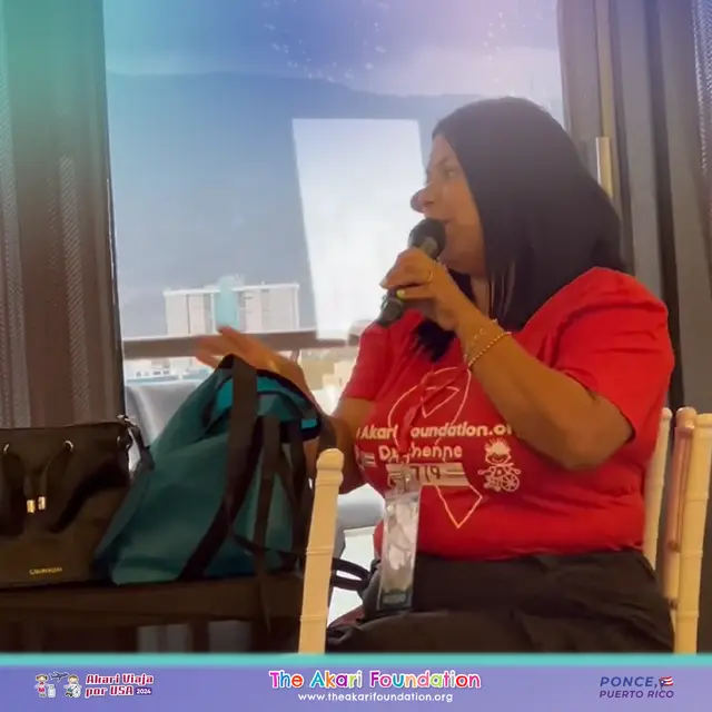 Una mujer con camiseta roja de The Akari Foundation habla al micrófono desde su silla.